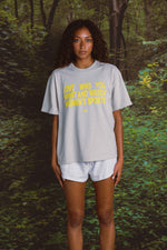 Person wearing a light gray t-shirt with yellow text in a forest setting
