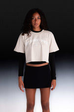 Person wearing a white crop top with text and black long-sleeve shirt underneath