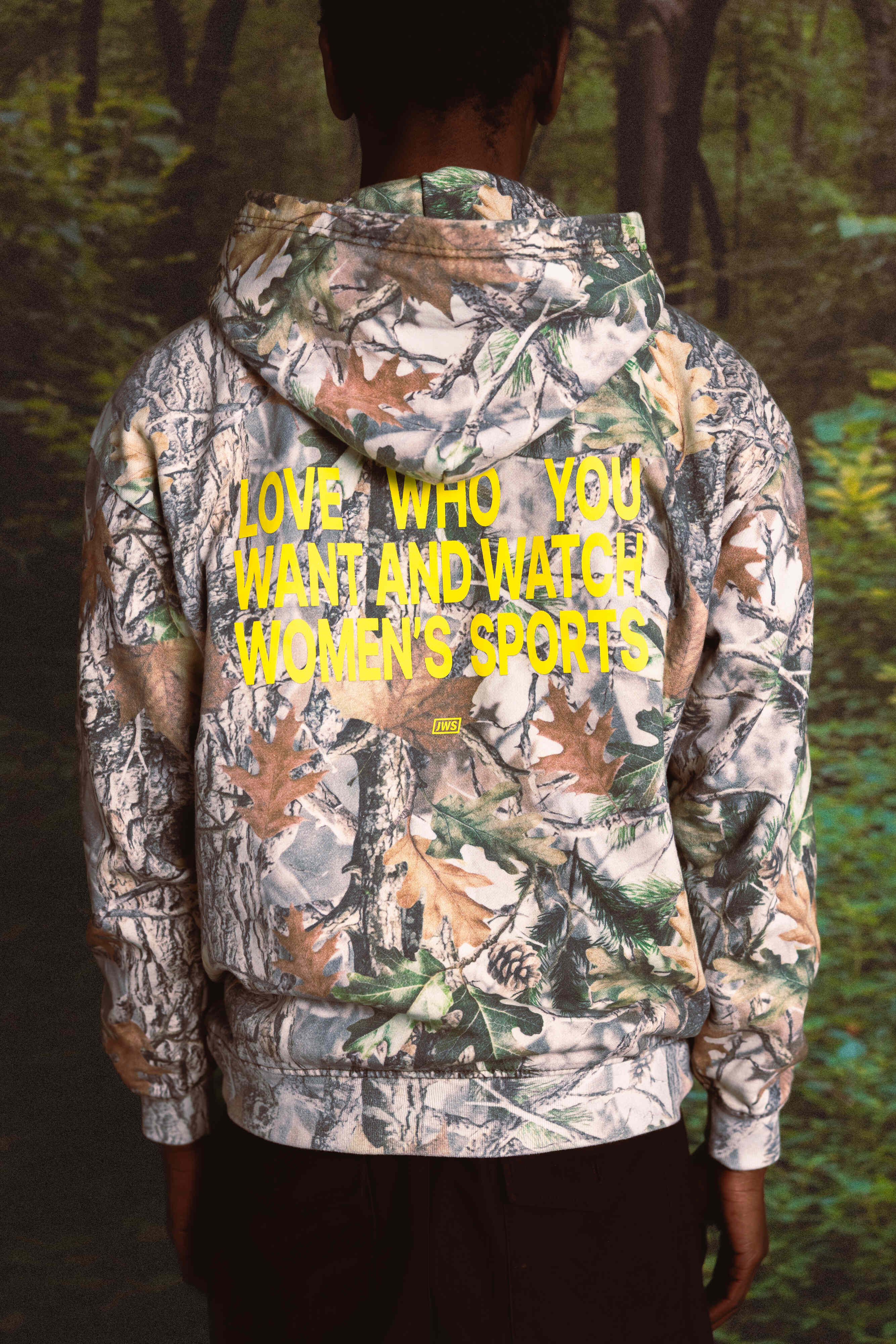 Person wearing a camouflage hoodie with text in a forest setting
