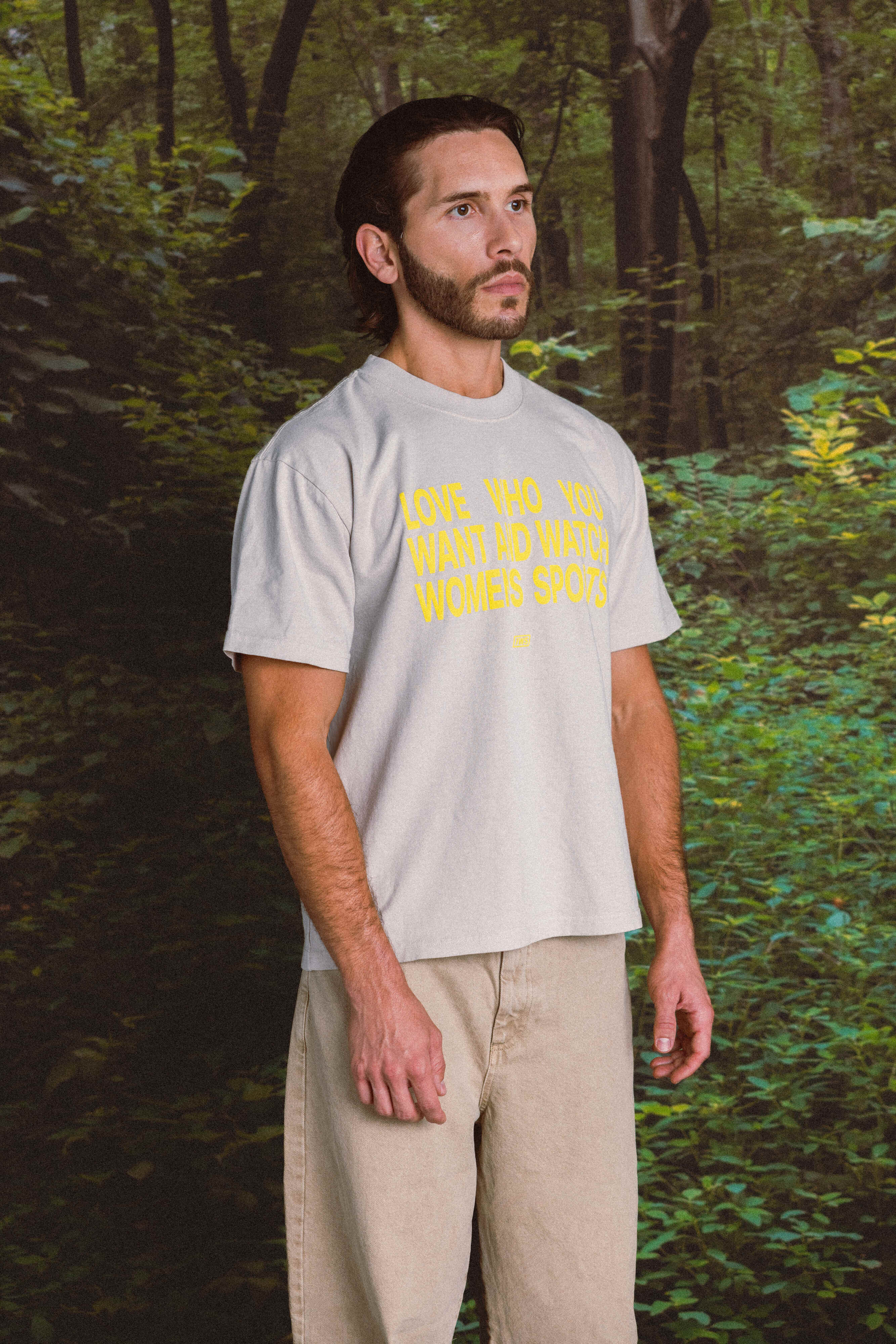 Person wearing a light gray t-shirt with yellow text in a forest setting