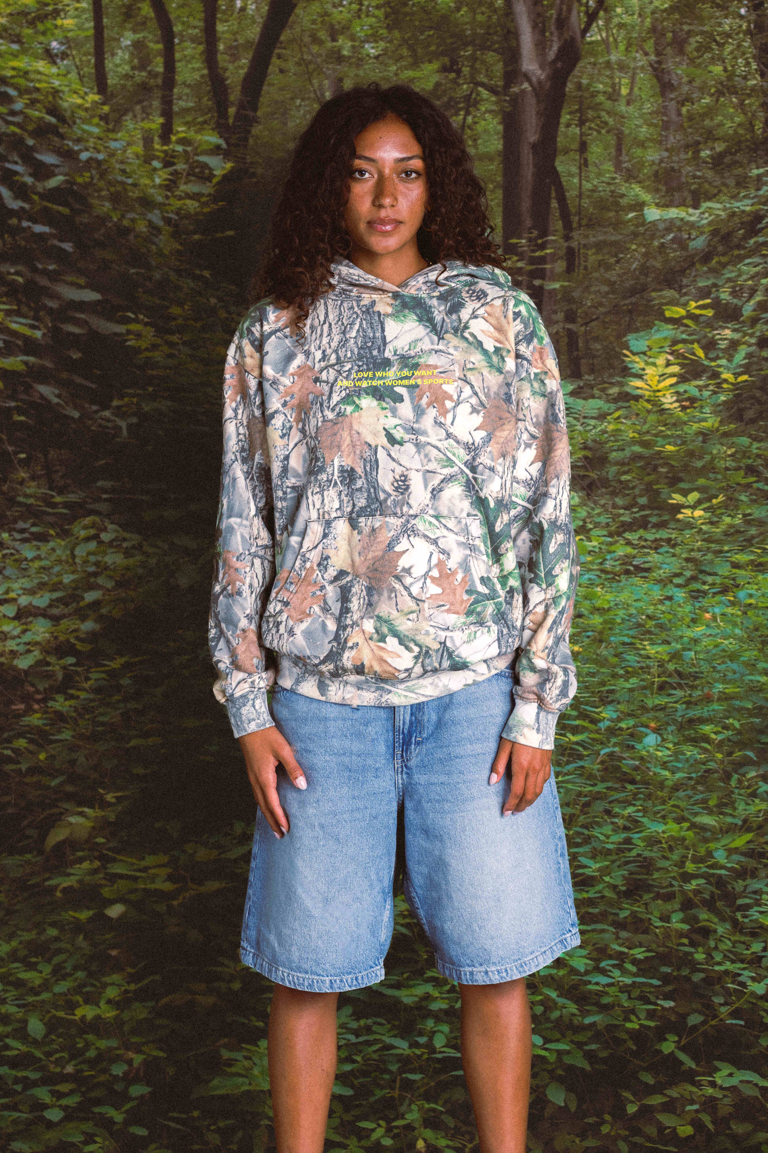 Person wearing a patterned hoodie and denim shorts standing in a forest
