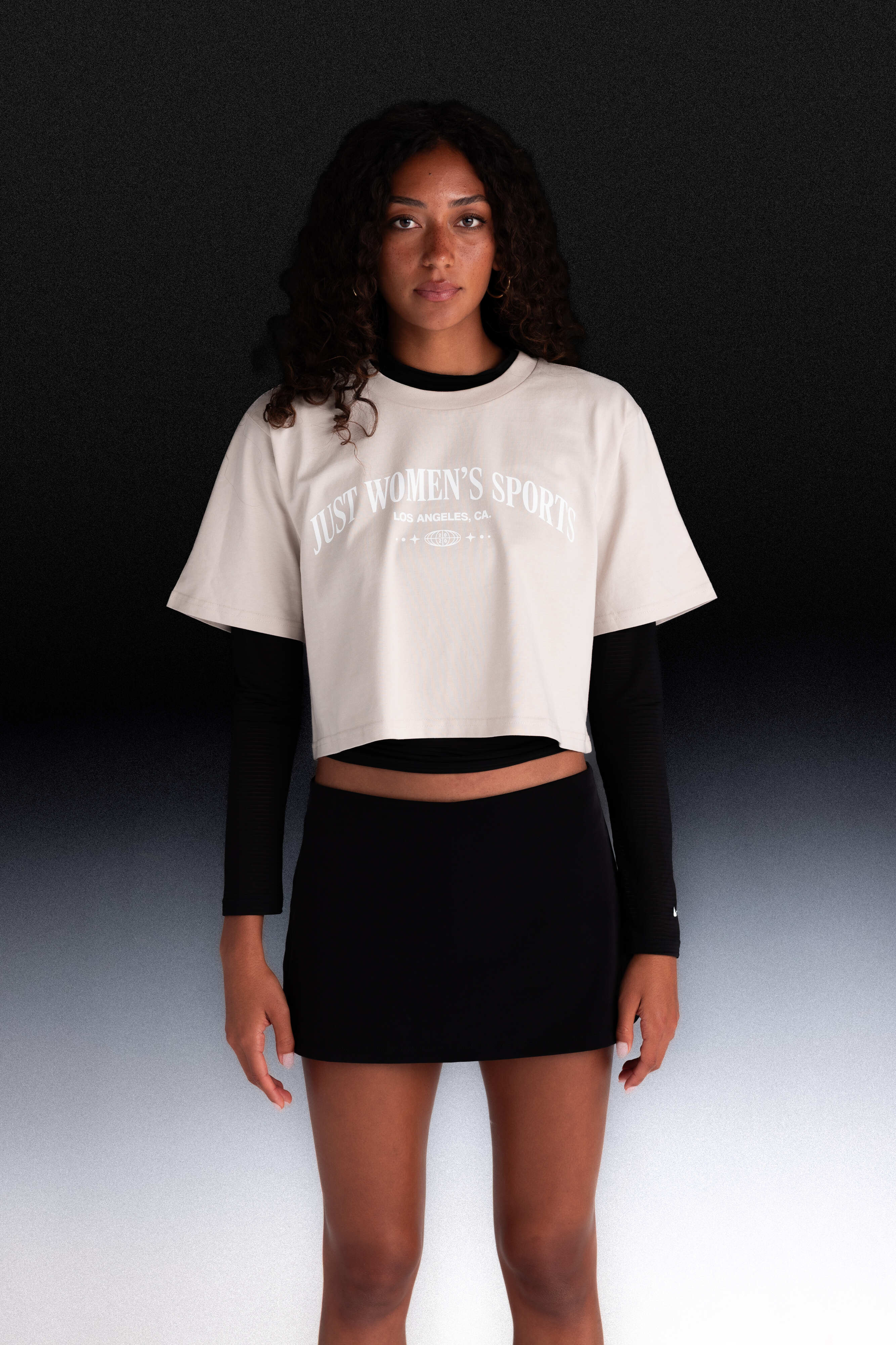 Person wearing a white crop top with text and black long-sleeve shirt underneath