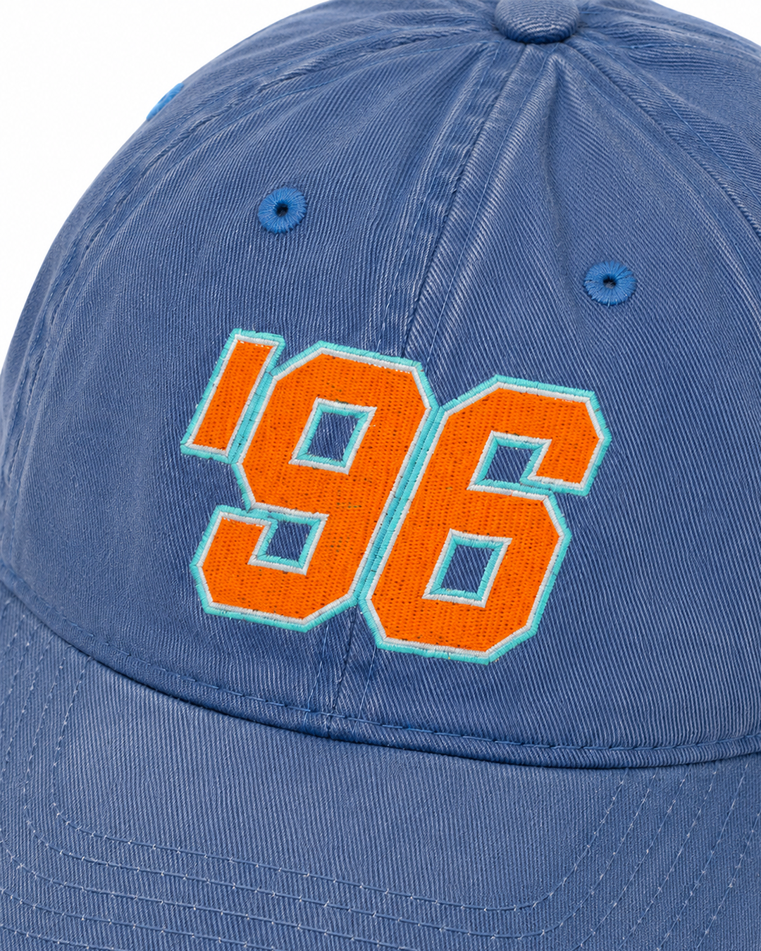 A close-up of a blue baseball cap featuring a large embroidered orange '96 with a light blue outline on the front panel.